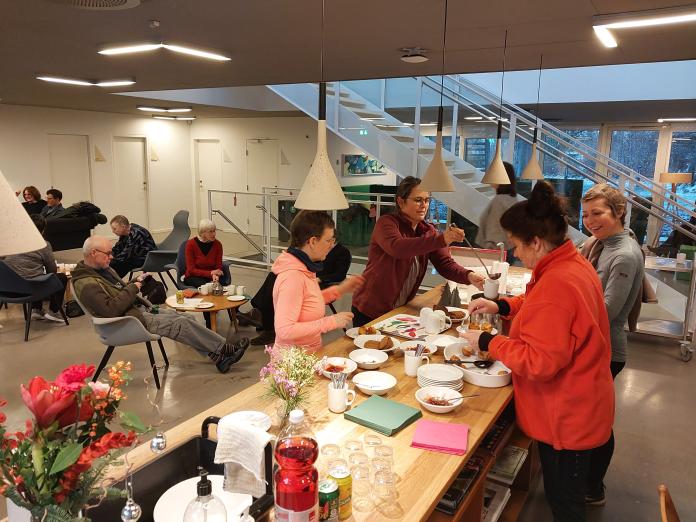 Fire personer står omkring et bord i Caféen i Center for Kræft og Sundhed og tager æbleskiver og gløgg.